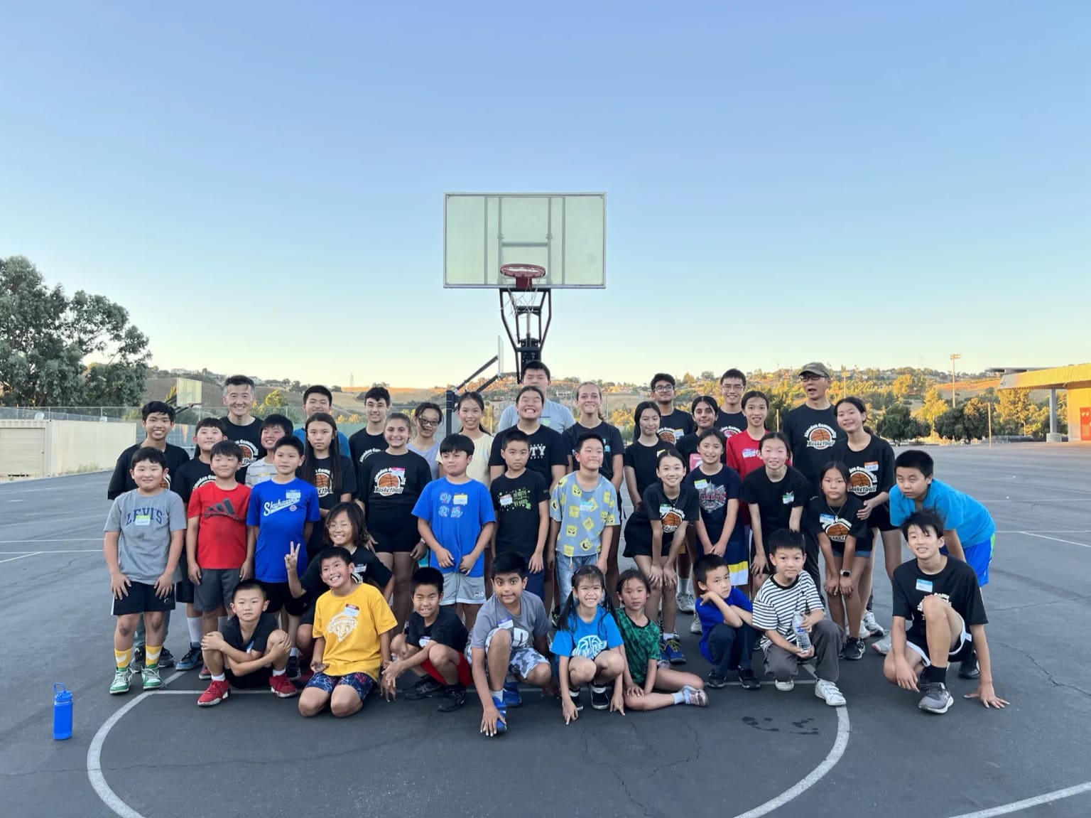 ACB players and coaches posing together under an outdoor hoop.