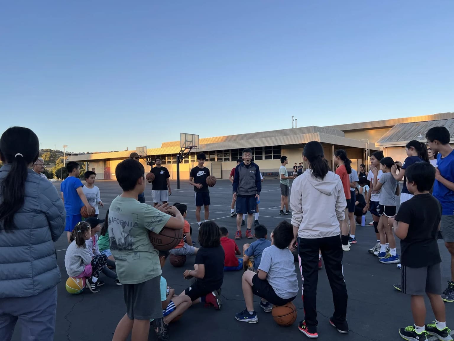 Players gathered around a coach on the outdoor basketball court.
